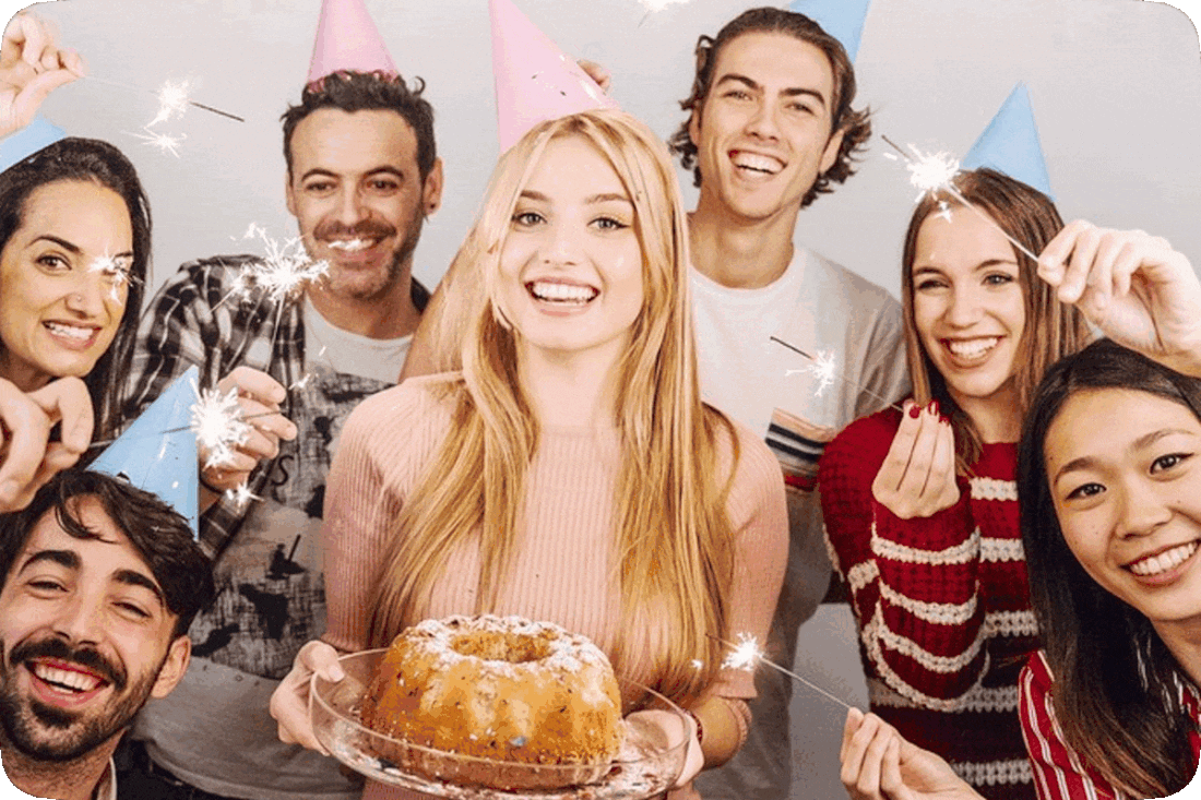Picture of a group of happy smiling young adults with one holding a cake and the rest holding lit sparklers.