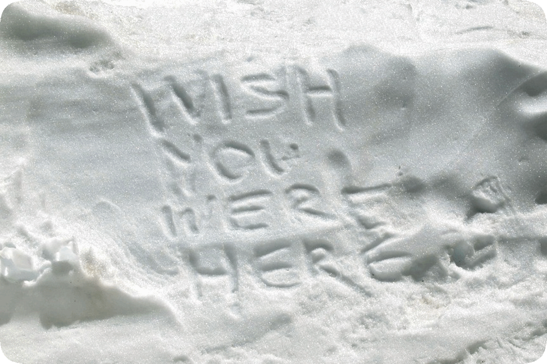 Picture of a snowbank with the words, ‘Wish You Were Here,’ written on it with a finger.